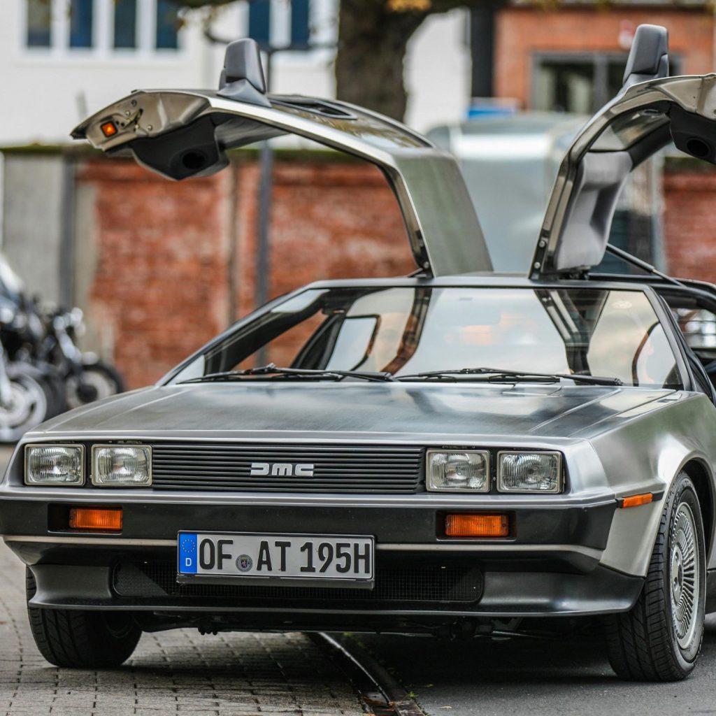 A DeLorean DMC-12 with gull-wing doors open is parked on a city street.