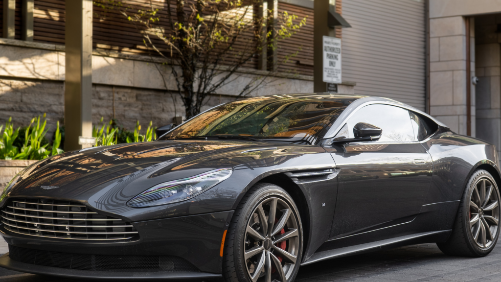A sleek, dark gray Aston Martin sports car is parked on a city street in front of modern buildings. The car's elegant curves, signature grille, and red brake calipers highlight its luxury and high-performance design. Dirt Legal can help register exotic vehicles like this, ensuring a hassle-free process so you can drive legally without DMV delays.