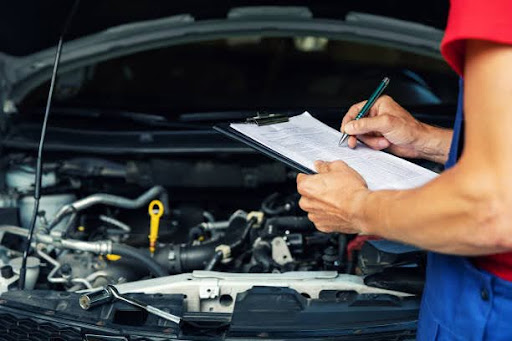 A mechanic inspecting a car engine while writing on a clipboard, documenting vehicle maintenance and repairs in an automotive service garage.