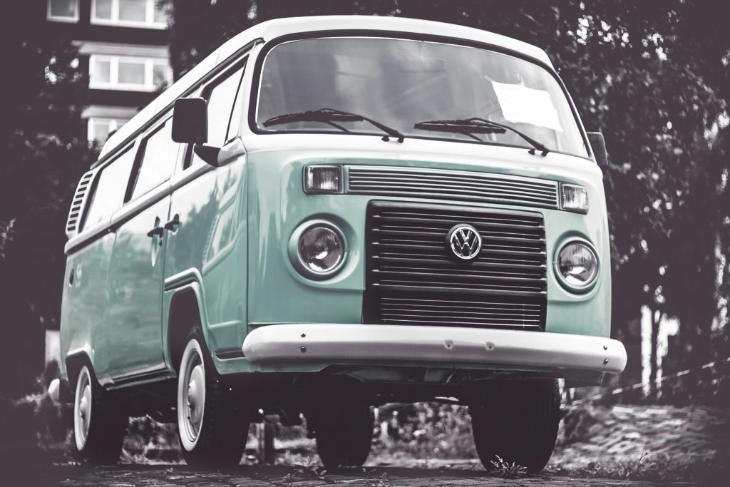 A vintage mint green Volkswagen van is parked on a quiet street surrounded by trees and buildings.