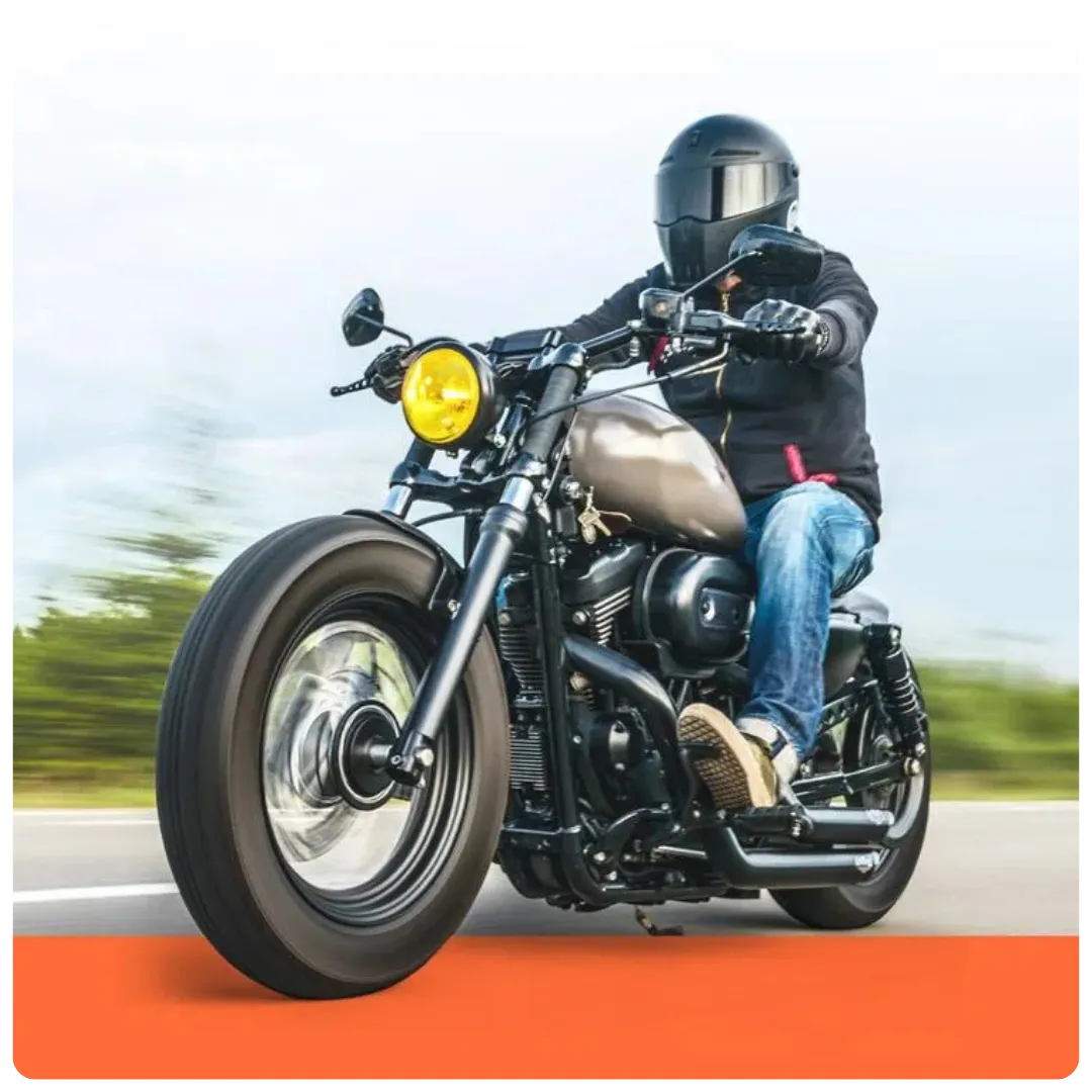 This image shows a motorcyclist wearing a black helmet and jacket riding a custom bobber-style motorcycle with a matte tank and yellow headlight on an open road.