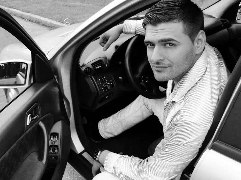 a man sitting in the driver’s seat of a car with the door open.