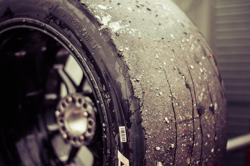 This is a close-up of a worn racing slick tire, covered in rubber debris and showing signs of heavy track use.