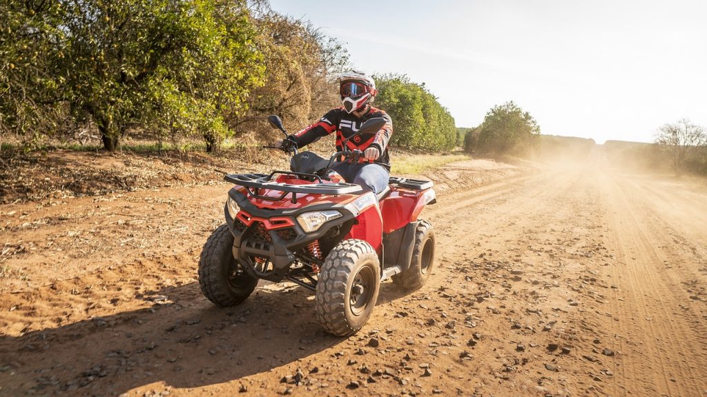 person riding a red all-terrain vehicle (ATV) on a dusty dirt road.