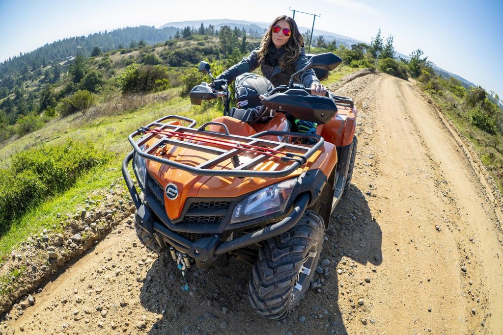 A confident rider pauses on a scenic dirt trail with her rugged orange quad—capturing the freedom and versatility that comes with owning a street legal ATV.