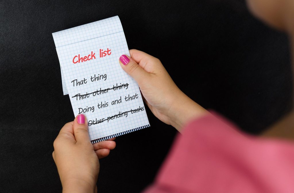 A person holds a notepad with a checklist representing what to do when selling a car.