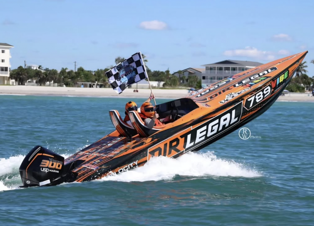 DirtLegal powerboat with two racers holding a checkered flag after winning the World Speedboat Championship on open water.