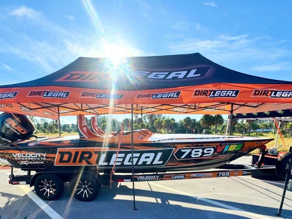 Dirt Legal-sponsored Velocity race boat displayed under a branded Dirt Legal canopy, highlighting the team’s presence at offshore racing events.