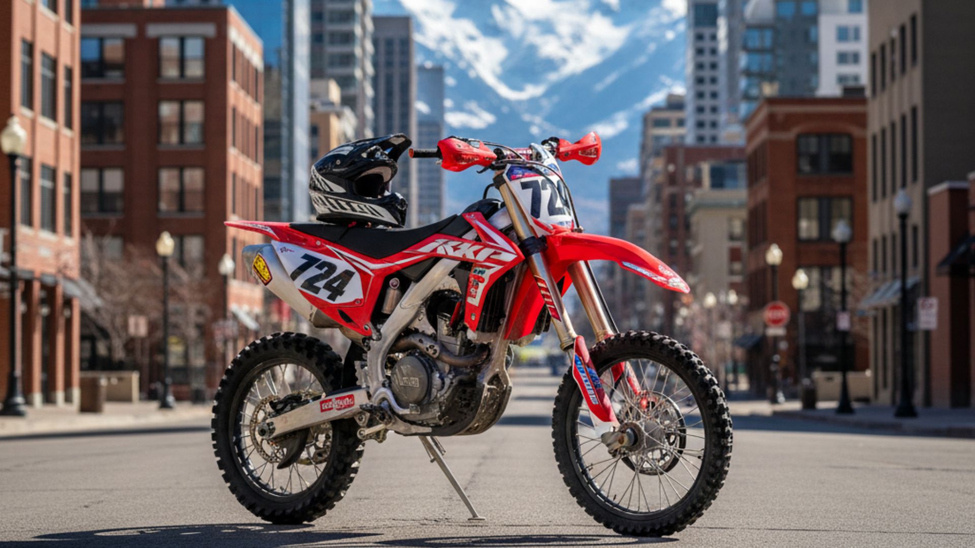 Dirt bike parked on a modern urban street in Salt Lake City, Utah, with a helmet resting on its seat, surrounded by glass buildings and distant mountains under a bright sky.
