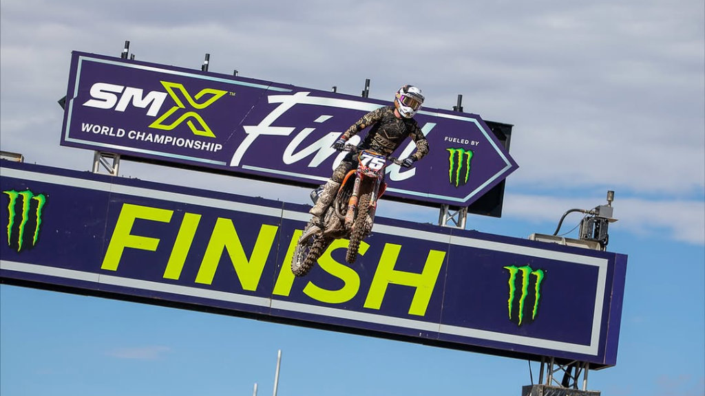 Motocross rider jumping over the SMX World Championship finish line banner fueled by Monster Energy.