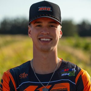 Headshot of Dirt Legal DBDRacing WMR KTM team rider Marcus Phelps smiling in his orange and black gear and team cap.